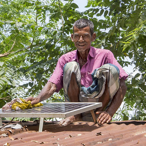 Mit Solaranlagen gegen Armut und für das Klima Solaranlagen gegen Armut und den Klimawandel: Ein älterer Mann installiert in Bangladesch ein Solarpanel auf dem Dach seines Hauses