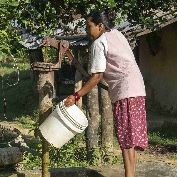 Sauberes Wasser ist für alle Lebensbereiche von größter Bedeutung Nepal: Frau füllt an einem Brunnen Wasser in einen Eimer