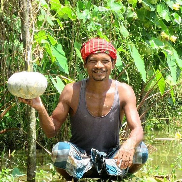 Bangladesch: Mann sitzt auf dem Boden im Garten und hält Gemüse hoch