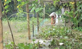 Eine Frau hat bis zur Brust das Wasser stehen. Sie watet durch den überfluteten Garten. Die Menschen aus den Dörfern ziehen in die Notunterkünfte in Chilmari.