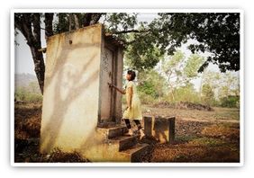 Mädchen vor Toilettenhäuschen in Indien