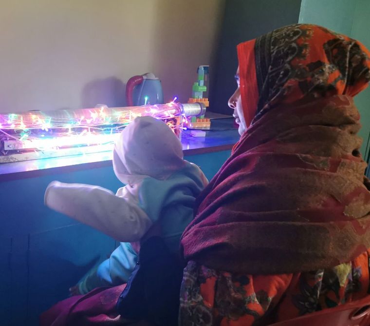 Augenlicht retten: Mutter sitzt mit ihrem Baby vor einer blinkenden Lichterkette