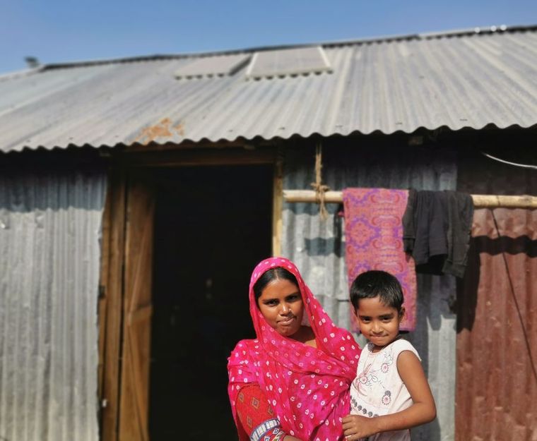 Bangladesch: Frau mit Kind vor dem Haus mit Solaranlage