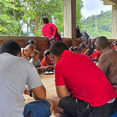 Nach der Flut in Nepal: Menschen versammeln sich in einem großen Raum, sitzen auf dem Boden und essen miteinander